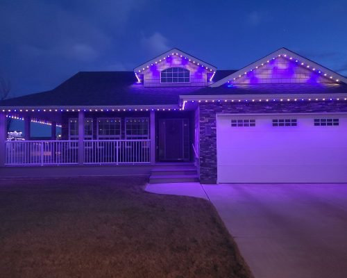 Stunning two-story home glowing with vibrant purple LED rope lights outlining rooflines, gables, porch railings, and garage at dusk. Professional holiday lighting installation by Spectrum Lighting Inc. – spectrumlightinginc.com.