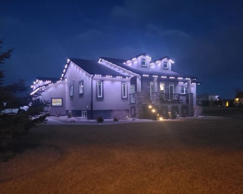 Stunning two-story home glowing with purple and white LED roofline holiday lights at night, professional Christmas light installation by Spectrum Lighting Inc., snowy yard, modern house exterior lighting display