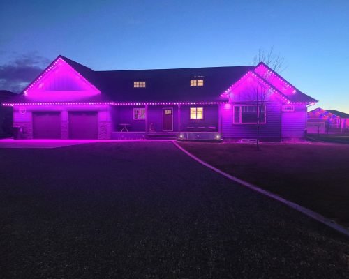 Vibrant purple LED roofline lighting on modern two-story home at dusk by Spectrum Lighting Inc. Magenta accent lights illuminate gables, garage doors, windows, and entryway for dramatic twilight glow, spectrumlightinginc.com outdoor home lighting installation.