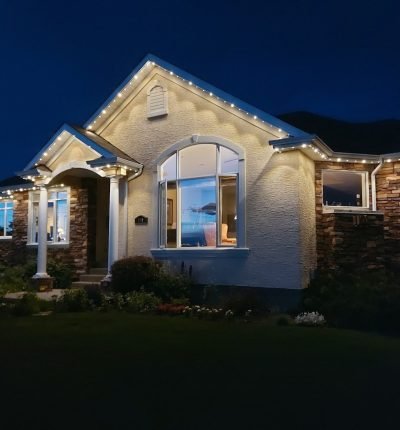 Stunning modern home exterior at night illuminated by professional LED landscape lighting from Spectrum Lighting Inc., featuring bright white accent lights along roofline, gables, large windows, stone accents, and porch for enhanced curb appeal