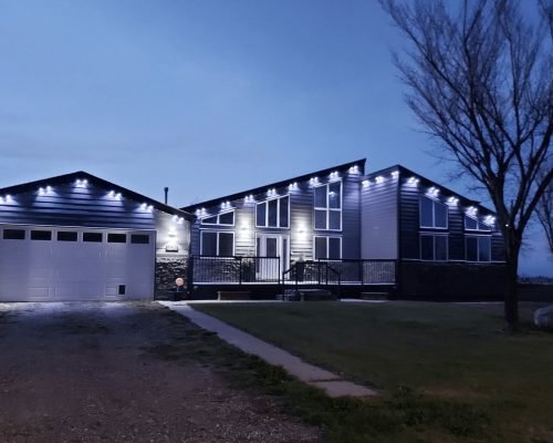 Modern angular home exterior with striking LED accent lighting along rooflines, eaves, and garage at dusk, highlighting contemporary architecture by Spectrum Lighting Inc.