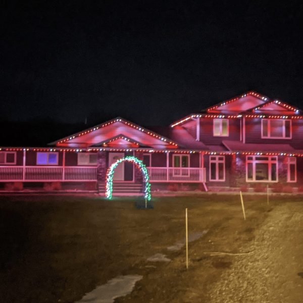 Vibrant pink holiday lights illuminating a large ranch-style house at night, featuring white roofline outlines, green arched entrance garland, and professional Christmas lighting installation by Spectrum Lighting Inc.