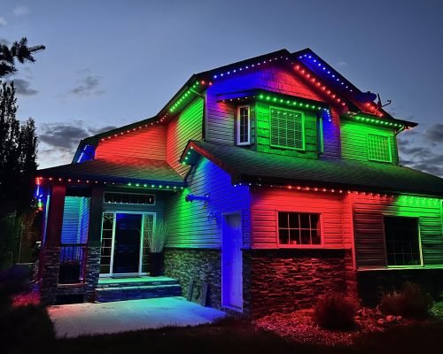 Vibrant RGB LED house lighting installation at dusk by Spectrum Lighting Inc., colorful red, green, blue permanent outdoor lights outlining modern two-story home architecture, roofline, windows, and foundation for stunning color-changing holiday display.